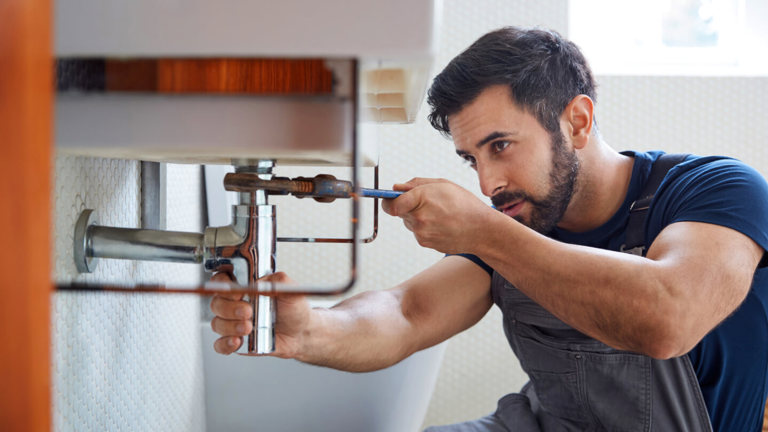 A man fixing a water leak under the bathroom sink.