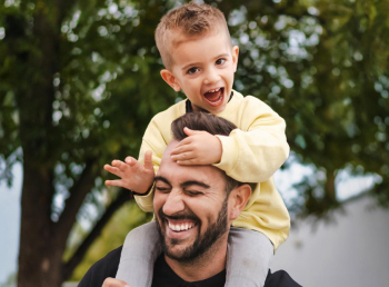 A picture of a man smiling while carrying his son on his shoulders