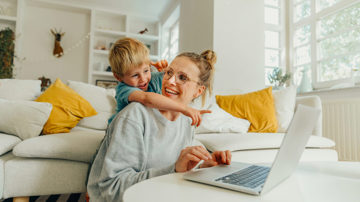 Woman looking into contents insurance on her laptop while being hugged by her child