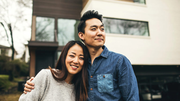 A couple posing in front of their house after purchasing contents-only insurance