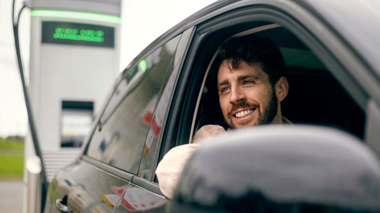 A male driver sitting in his electric car at an EV charging station