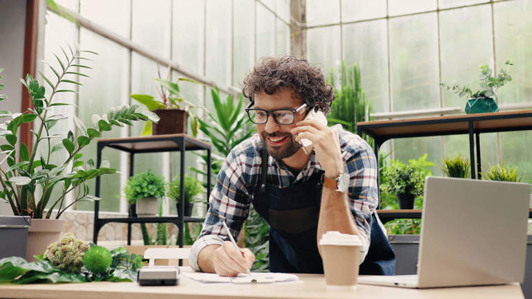 Image of a small business owner on the phone leaning on a bench.