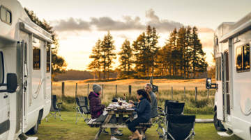 Three campers sitting at a picnic table between two used motorhomes