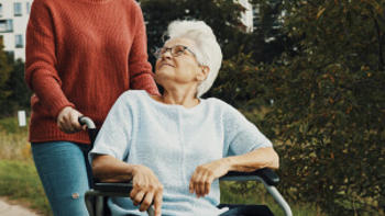 An elderly lady being wheeled in a wheelchair. 