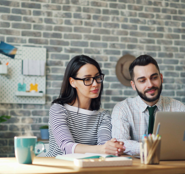 Two people sitting at a desk looking at a laptop.